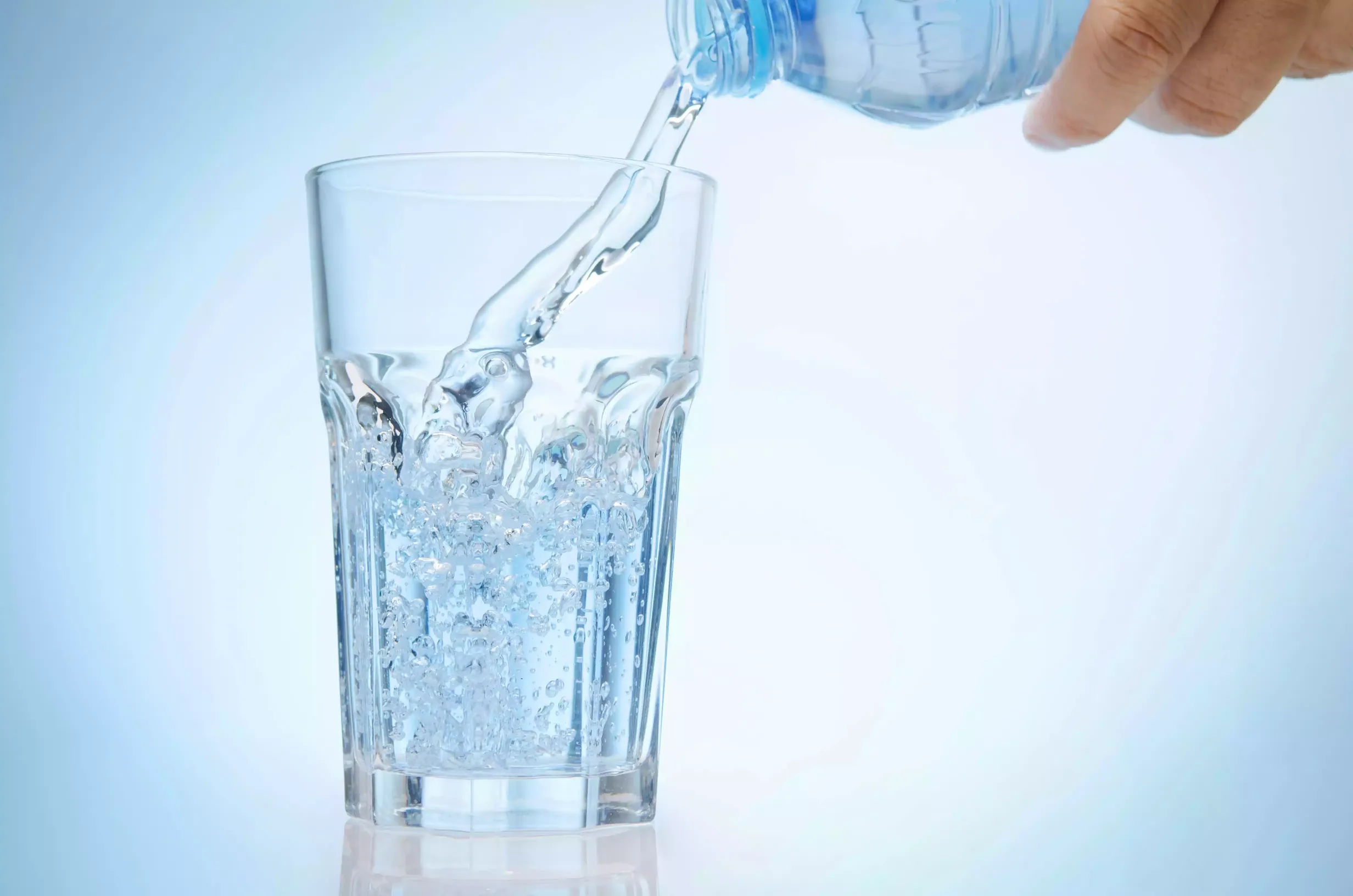A hand pours water from a plastic bottle into a clear glass, with water splashing and bubbles forming—refreshing relief for those experiencing dry mouth.
